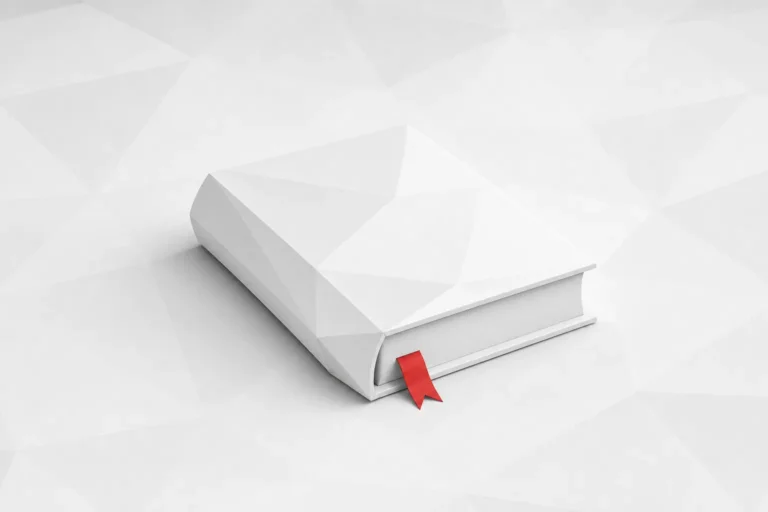 Libro de color blanco, cerrado y tumbado, con una cinta roja de marcapáginas asomando entre sus hojas