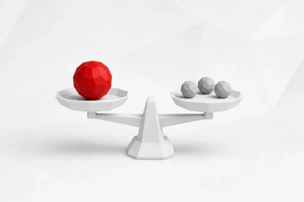 Balanza blanca facetada en equilibrio con una esfera roja grande en un platillo y tres esferas grises pequeñas en el otro