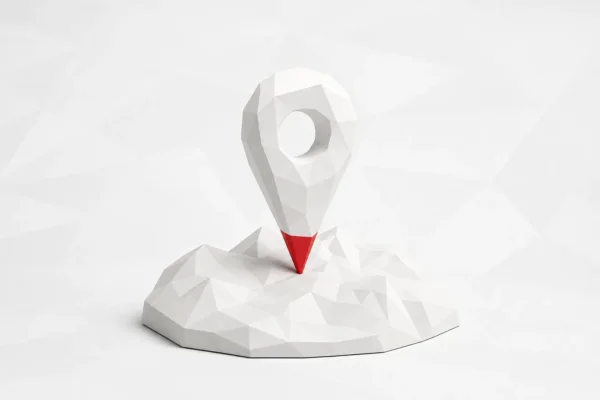 Un marcador de mapa facetado blanco con la punta roja, clavado sobre un relieve del mismo material