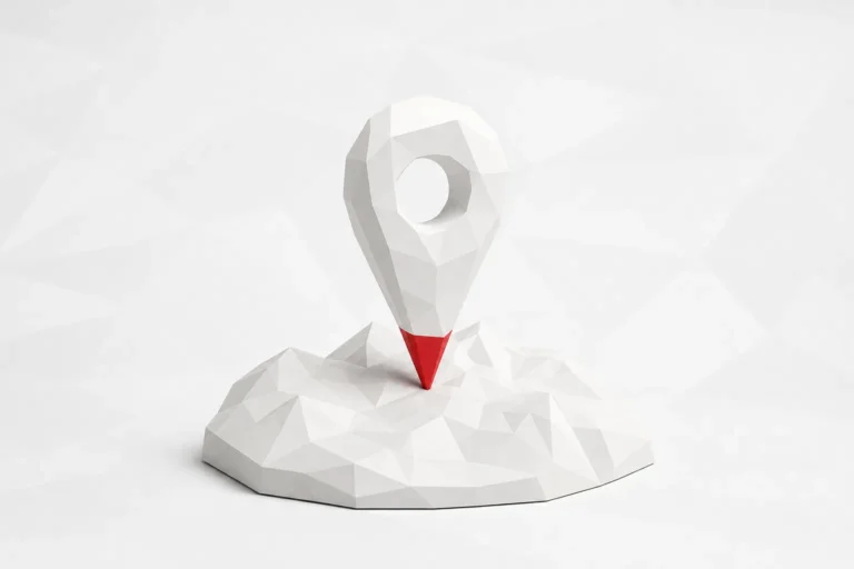 Un marcador de mapa facetado blanco con la punta roja, clavado sobre un relieve del mismo material