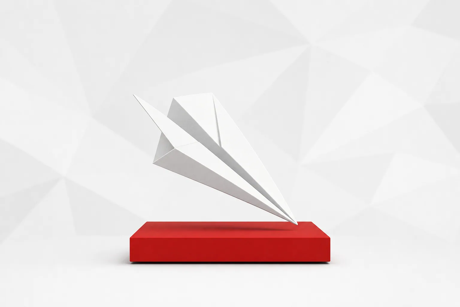 Avión de papel blanco que se posa de punta sobre un bloque rojo, ante un fondo gris claro de formas geométricas